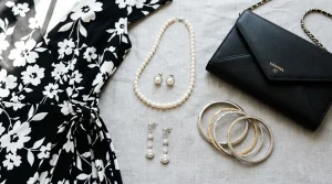 Black and white dress styling accessories flat lay with pearl necklace, earrings, clutch, and bangles